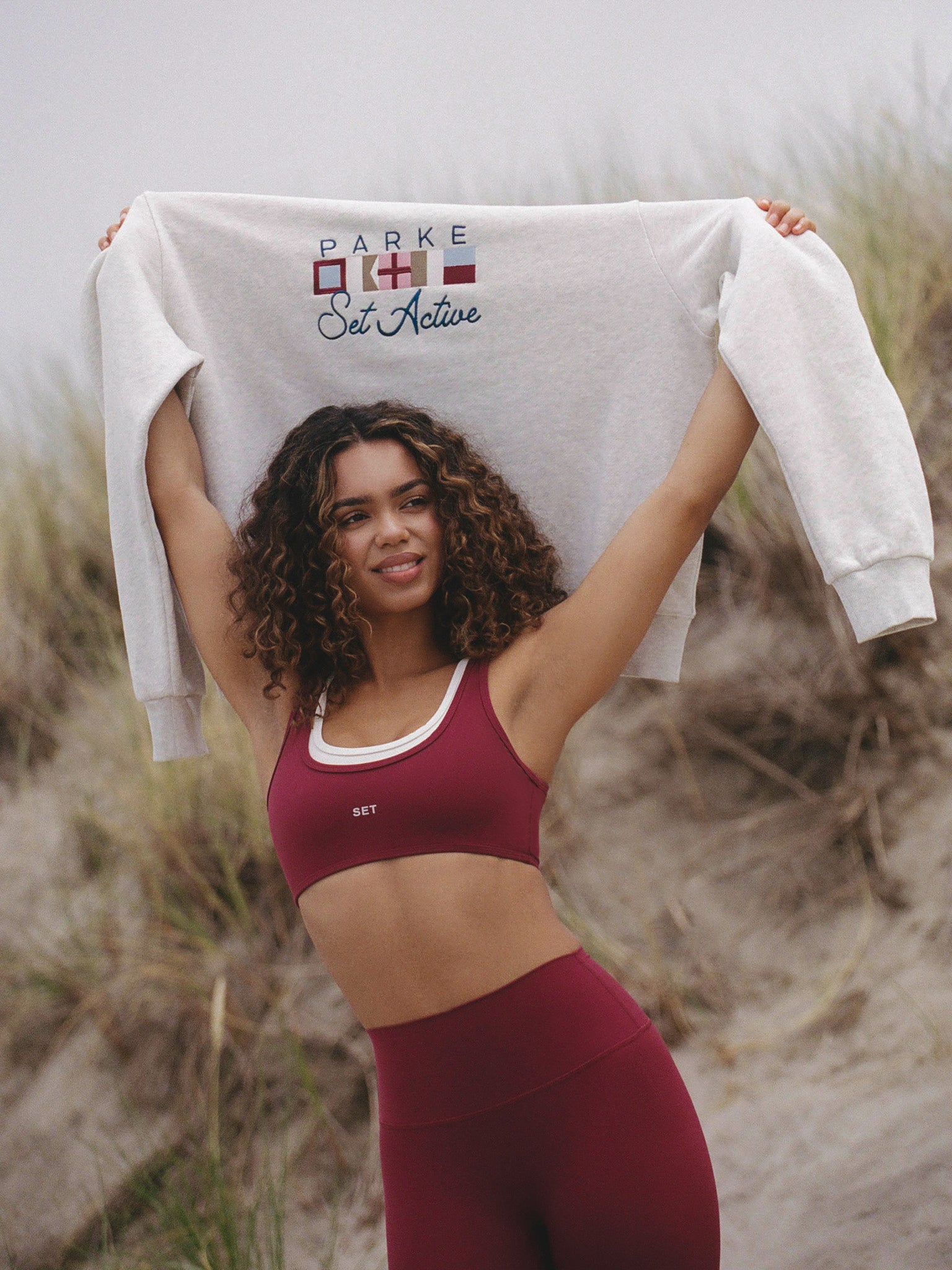 Woman holding a sweatshirt with 'Parke Set Active' branding in an outdoor setting