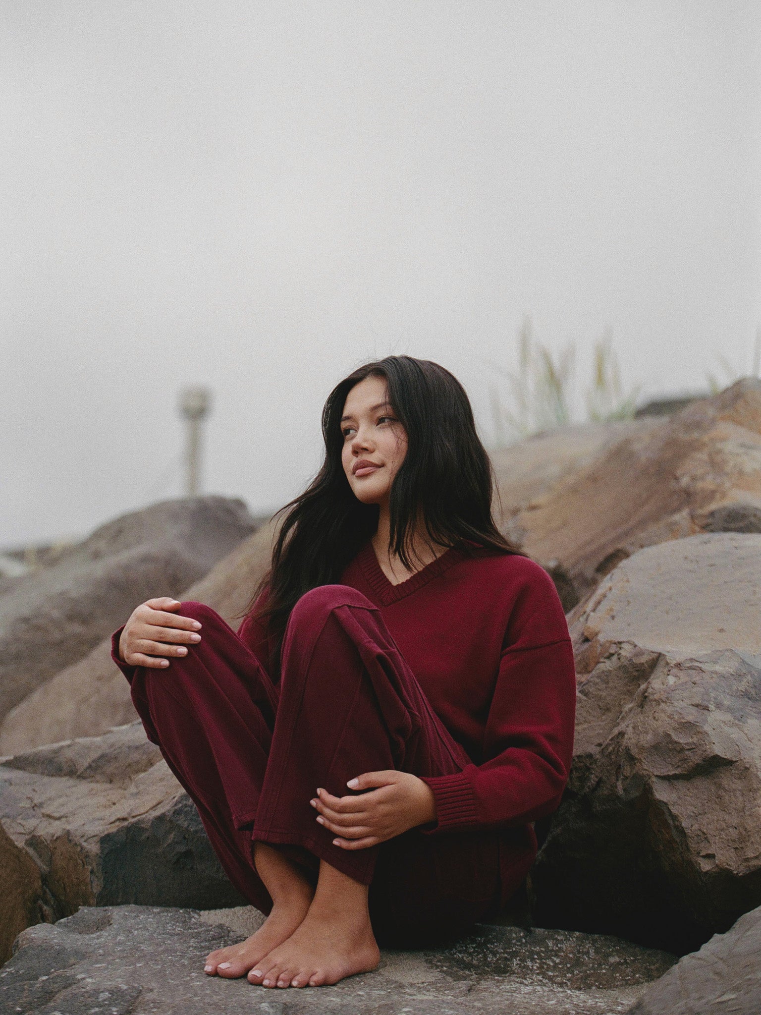 Woman in a red outfit sitting on rocks with a misty background