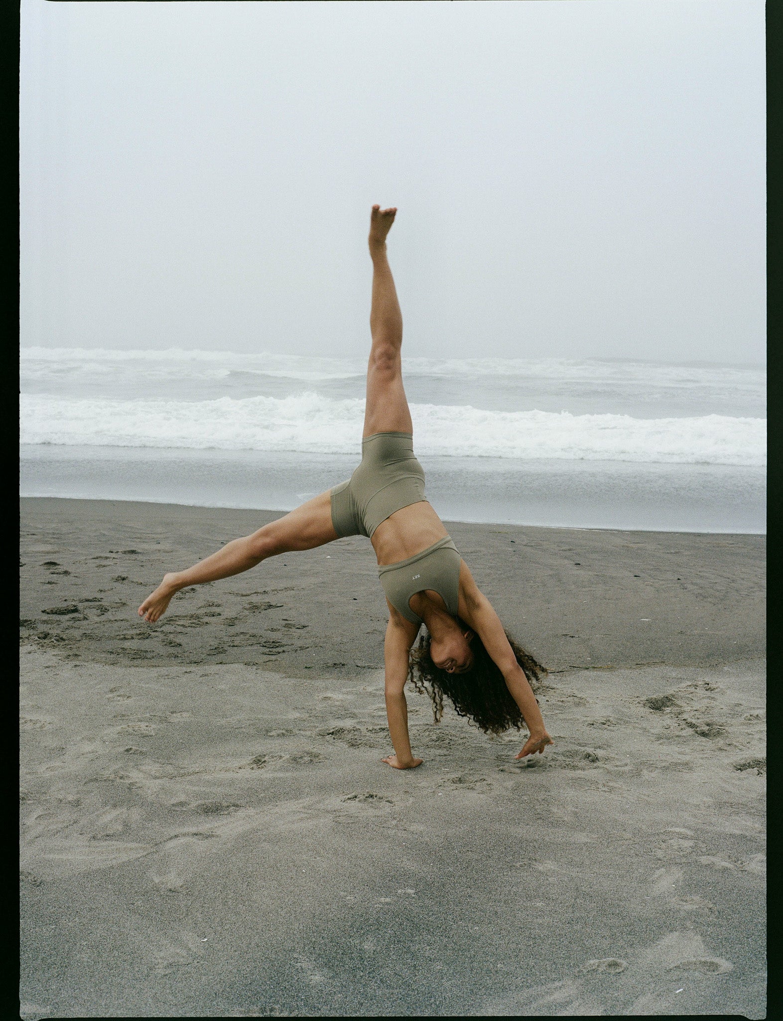 Person doing a handstand on a beach with ocean waves in the background