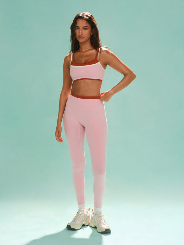 Woman wearing a pink sports bra and leggings set on a light green background