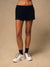 A model from the waist down wearing black athletic shorts, black crew socks, and white trail running shoes against a neutral beige studio background.