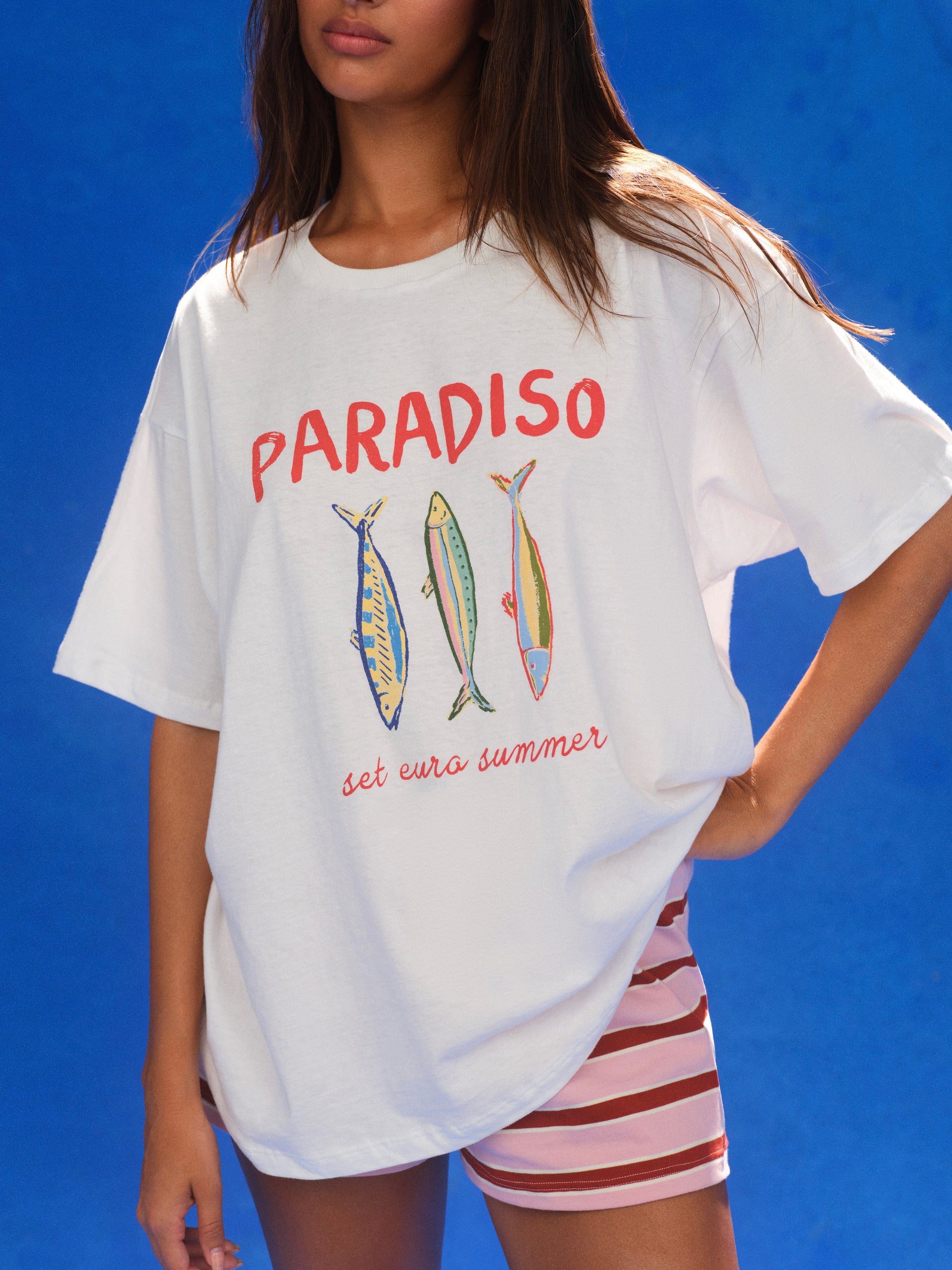 Person wearing a white t-shirt with 'Paradiso' and fish illustrations on a blue background