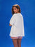 Woman wearing a white oversized shirt and red striped shorts against a blue background