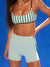 Person wearing a green and white striped bikini top and light blue shorts against a blue background
