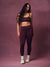 A woman modeling a matching burgundy activewear set consisting of a sports bra and high-waisted leggings, paired with white socks and sneakers, set against a solid textured mauve studio backdrop. <model-info> Christina wears a size L and is 5’9, 29½” waist, 36" bust.</model-info> 