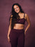 A woman modeling a matching burgundy activewear set consisting of a sports bra and high-waisted leggings, posed against a solid mauve studio backdrop. <model-info> Christina wears a size L and is 5’9, 29½” waist, 36" bust.</model-info> 
