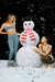 Two people in workout attire standing next to a snowman with a red scarf on a snowy background.