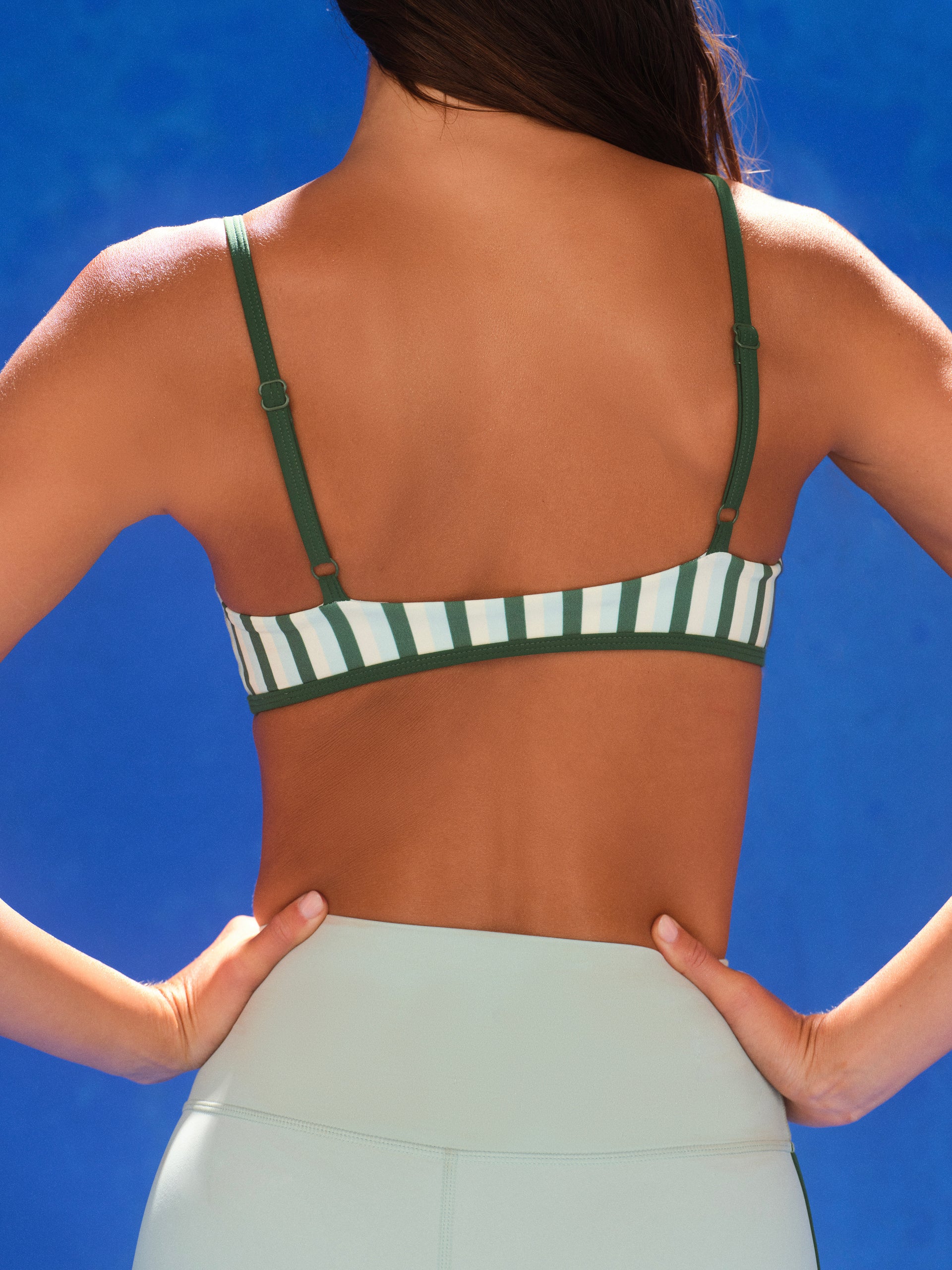 Person wearing a green and white striped sports bra against a blue background