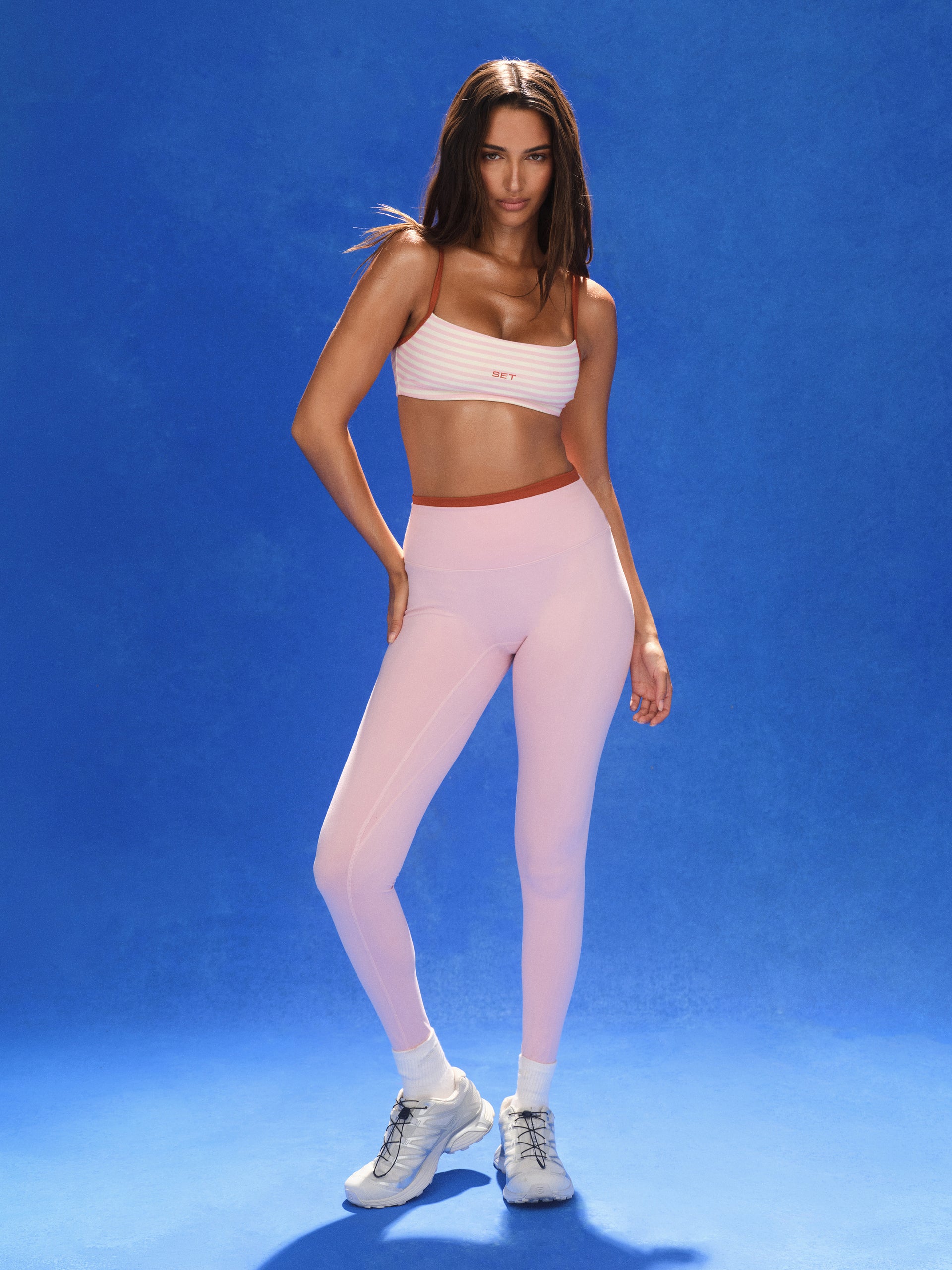Woman wearing a white sports bra and pink leggings on a blue background