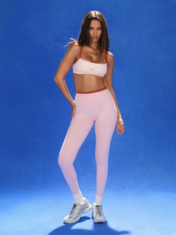 Woman wearing a white sports bra and pink leggings on a blue background