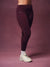 A person wearing high-waisted burgundy athletic leggings with a decorative side stripe and a small white 'SET' logo, paired with white socks and off-white sneakers, against a solid mauve studio backdrop.