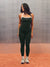 A woman modeling a matching black athletic set consisting of a tank top and leggings, featuring white trim and side stripes, standing on a terracotta-colored floor against a textured gray backdrop.  <model-info>Alana wears a size M and is 5’8”, 28” waist, 35" bust.</model-info>backdro