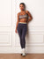 A woman stands against a white paneled wall wearing a grey and beige striped sports bra and matching grey leggings, with white socks and white sneakers. <model-info>Courtney wears a size S and is 5’8”, 25” waist, 32B bust.</model-info>