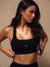 A woman wearing a black scoop-neck athletic sports bra with a small white 'SET' logo on the front, posed against a warm beige studio background. <model-info>Jelene wears a size XS and is 5’7”, 23” waist, 32AB bust.</model-info>