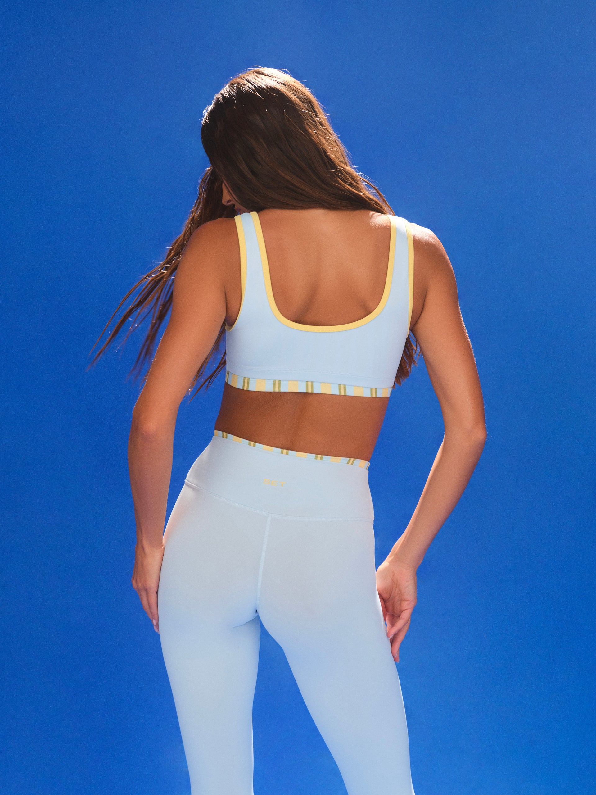 Woman wearing a light blue sports bra and leggings set against a clear blue sky.