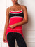 A woman wearing a red, black, and white athletic set consisting of a scoop-neck tank top and matching high-waisted leggings, standing against a white paneled wall.