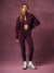 A woman modeling a matching burgundy athletic set consisting of a zip-up jacket and leggings, styled with white sneakers against a textured mauve studio backdrop. <model-info> Andrea wears a size S and is 5’9”, 25½” waist, 32” bust.</model-info>