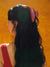 Person with long dark hair wearing a red and blue plaid hair clip against an orange background
