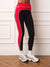 A person wearing high-waisted athletic leggings in red, black, and gray side panels, paired with white socks and white sneakers, standing against a white paneled wall.