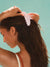 Woman using a pink claw clip on her hair against a light blue background