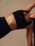 A close-up of a woman wearing a black athletic sports bra with a small white 'SET' logo on the side, shown against a warm beige background.