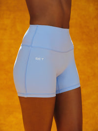 Side view of Aeraline Breathe Pipe shorts in Popsicle showing high-rise fit, tonal piping, and visible SET logo on orange background