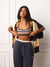 A woman modeling a matching athletic set from the brand Fila, featuring a navy blue sports bra with beige and white stripes, navy blue sweatpants with a cream waistband, and a navy and cream striped cardigan draped over her shoulders.