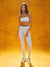 Woman wearing a white sports bra and leggings set against an orange background