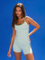Woman wearing a light green tank top and shorts against a blue background <model-info>Kushi wears a size S and is 5'8, 24” waist, 32C bust.</model-info>
