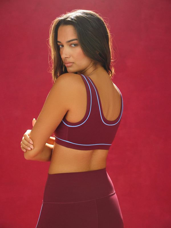 Woman wearing a maroon sports bra and leggings against a red background