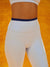 White leggings with a navy waistband on a blurred orange background