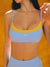 Woman wearing a blue and yellow sports bra with 'SET' branding against an orange background <model-info>Jasmine wears a size S and is 5'8, 25” waist, 32C bust.</model-info>