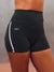 Close-up of a model wearing black high-waisted athletic shorts with a white side stripe and the brand name 'SET' printed in white on the hip, against a neutral gray background. <model-info>Scha'leigh wears a size XS and is 5’8”, 24” waist, 32B bust.</model-info>
