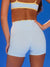 Person wearing light blue shorts with a brown top against a blue background <model-info>Logan wears a size XS and is 5’9½”, 24” waist, 32B bust.</model-info>
