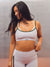 A woman modeling a matching athletic set featuring a light pink sports bra with dark green trim and matching high-waisted leggings with green side panels, set against a gray studio background. <model-info>Alana wears a size M and is 5’8”, 28” waist, 35" bust.</model-info>