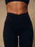Close-up of a model's midsection wearing high-waisted black athletic leggings and a matching black sports bra against a warm beige studio background.