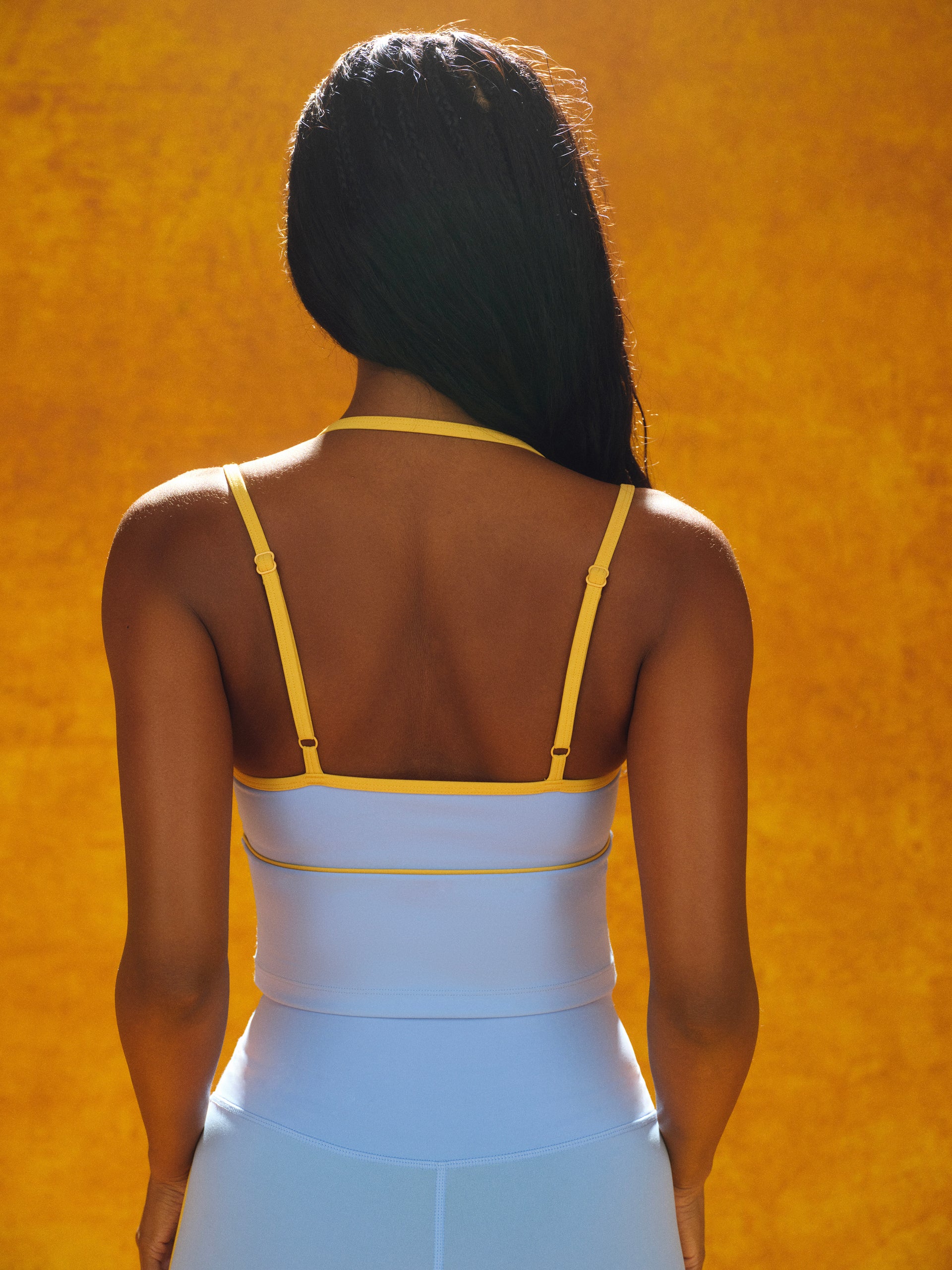 Person wearing a white dress with yellow straps against an orange background