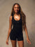 A woman modeling a black sleeveless bodysuit with short legs and a scoop neckline, featuring a small white 'SET' logo on the chest, set against a textured warm gray studio backdrop. <model-info>Lena wears a size XS and is 5’7”, 24½” waist, 31" bust.</model-info>