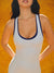 Woman wearing a white tank top with blue trim against an orange background