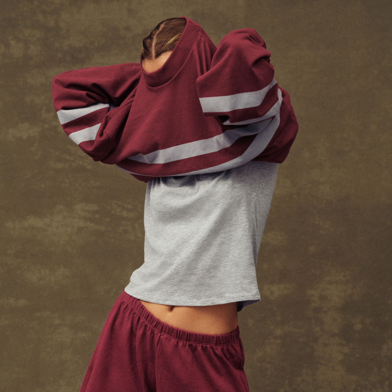 Person wearing a burgundy and gray tracksuit against a brown background