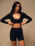 A woman modeling a black long-sleeve crop top and matching high-waisted biker shorts against a plain beige studio background. <model-info>Jelene wears a size XS and is 5’7”, 23” waist, 32AB bust.</model-info>