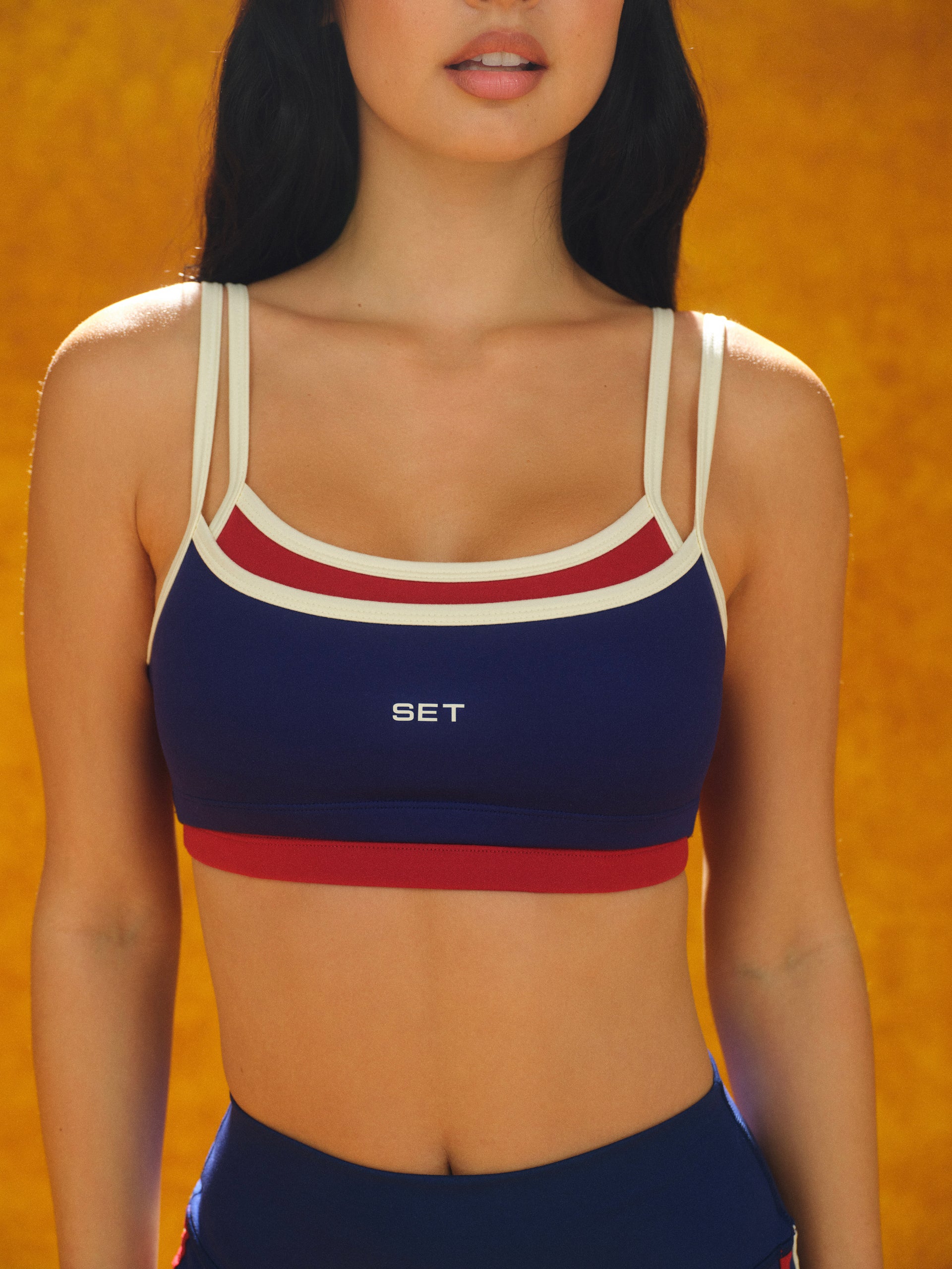 Person wearing a blue and red sports bra with 'SET' branding against an orange background