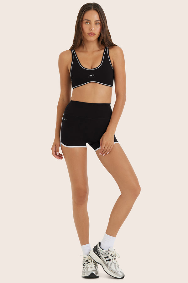 Woman wearing a black sports bra and shorts set on a beige background