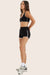 Woman wearing a black sports bra and shorts set on a beige background