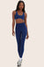 Woman wearing navy blue sports bra and matching high-waisted leggings with blue piping, both branded 'SET' on chest and thigh, paired with white socks and sneakers.