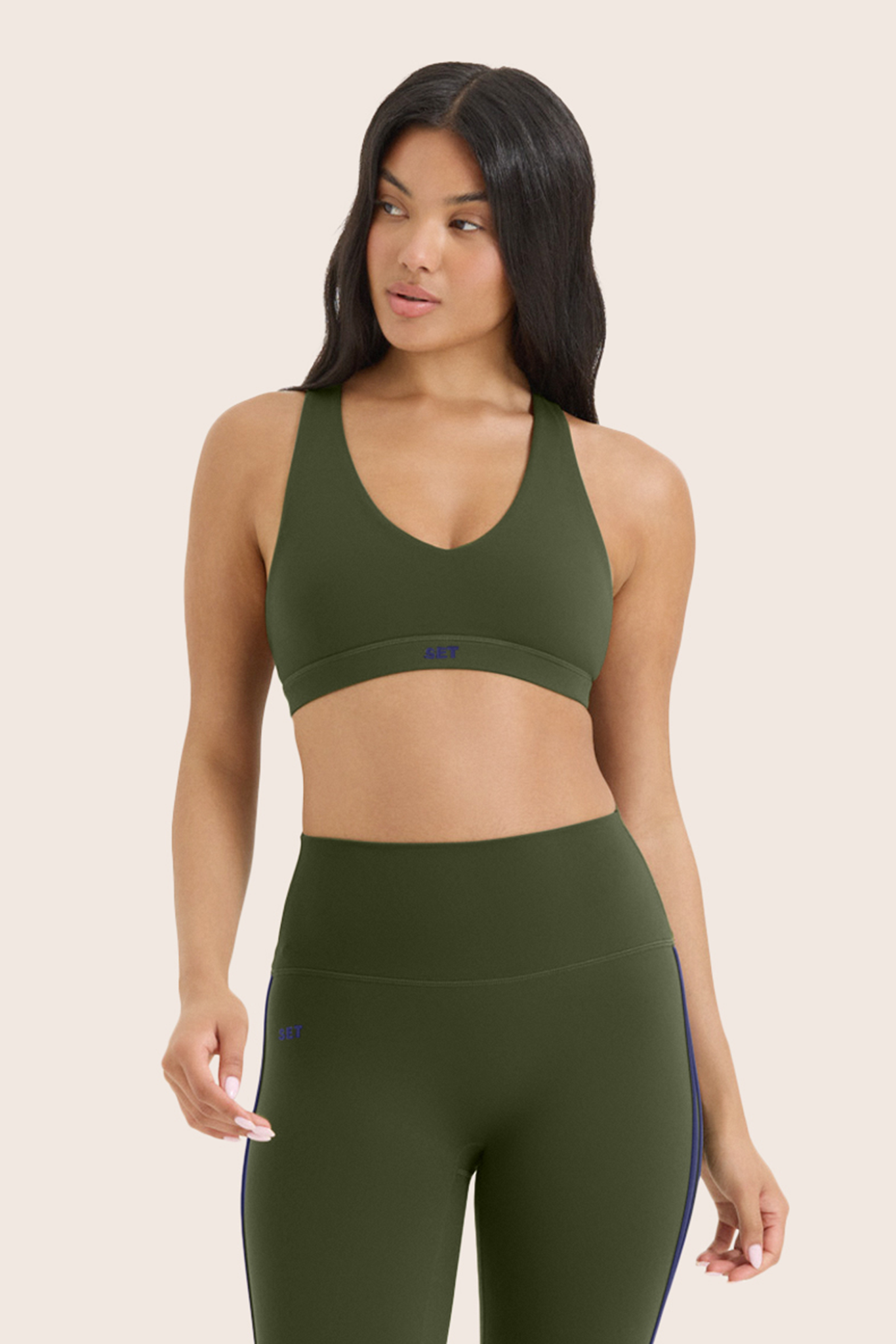 Woman wearing an olive green sports bra and leggings set on a beige background 