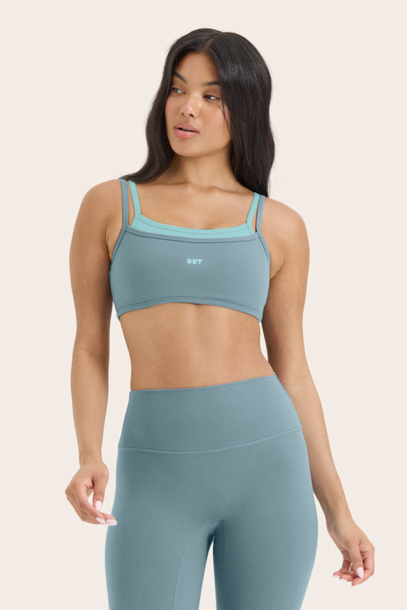 Woman wearing a teal sports bra and leggings on a beige background 