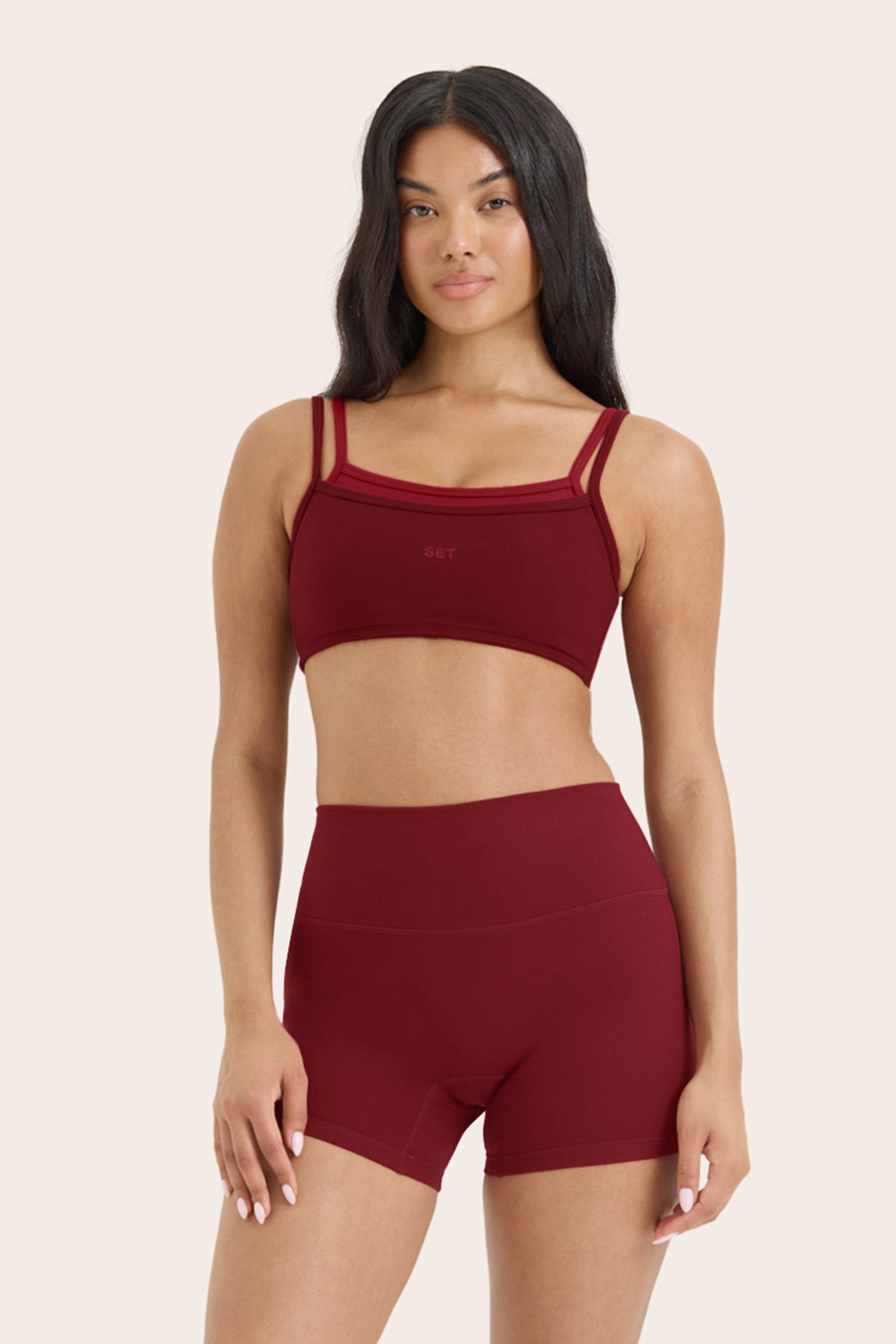 Woman wearing a burgundy sports bra and shorts set on a beige background 