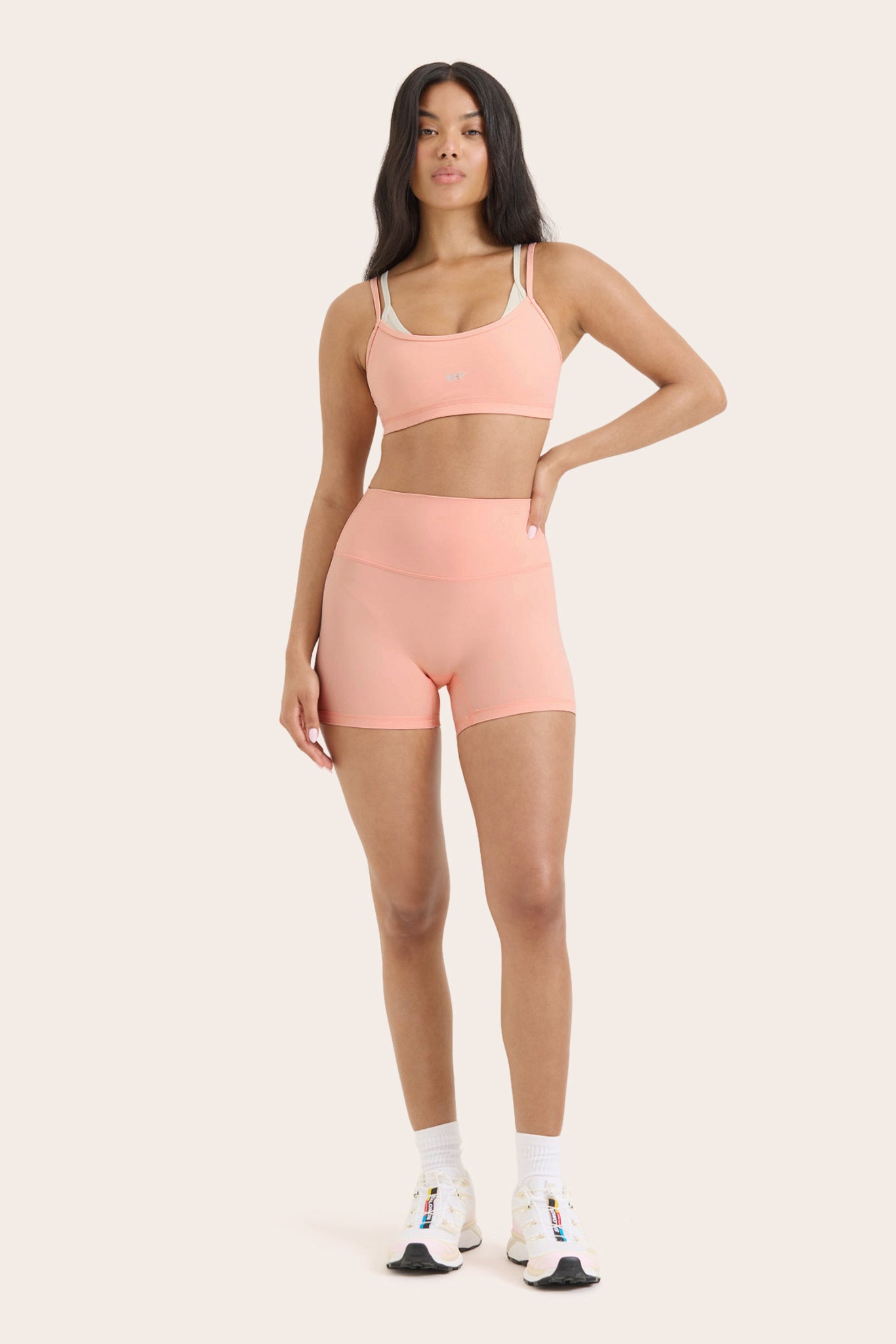 Woman wearing a pink sports bra and shorts set on a white background