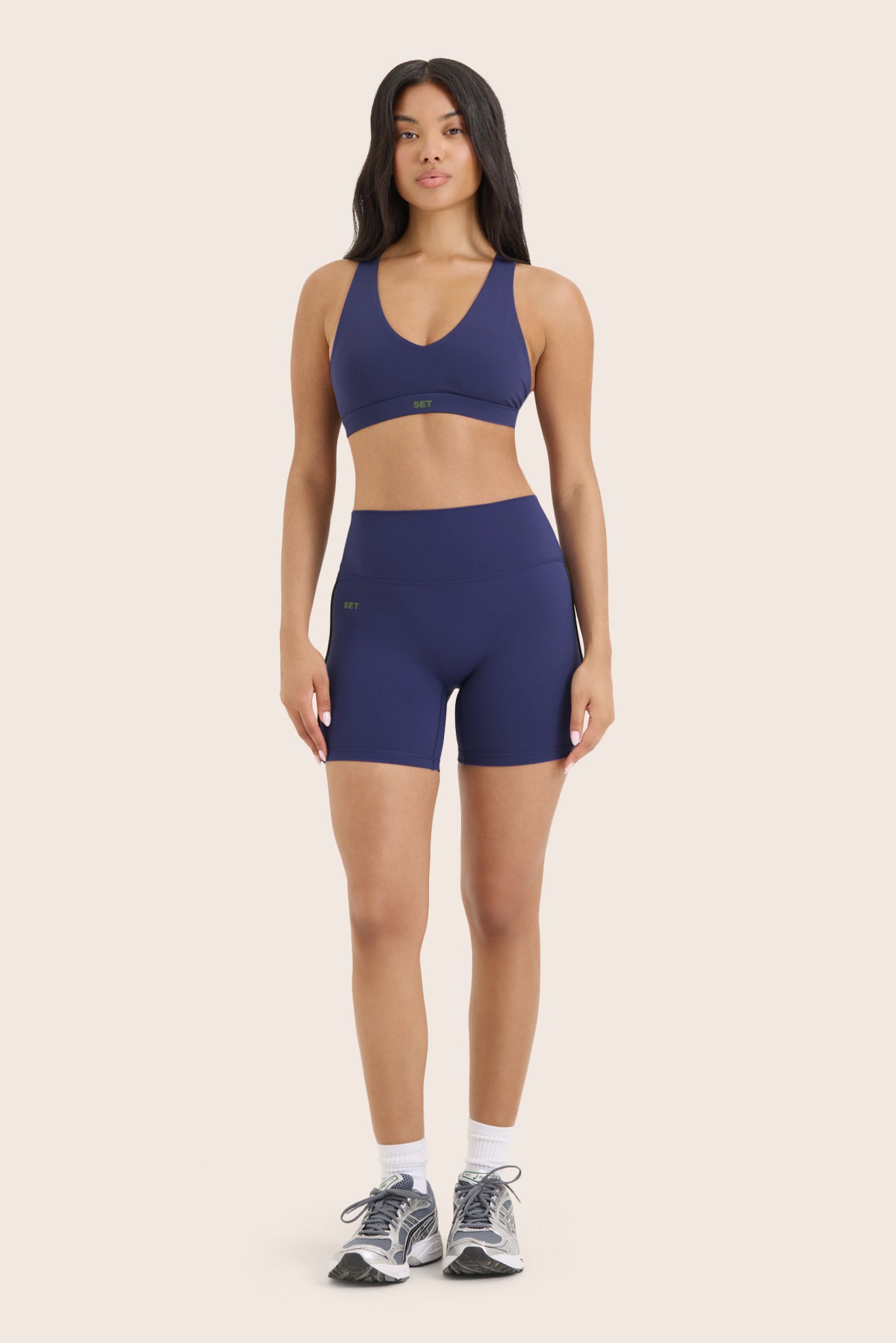 Woman wearing a blue sports bra and shorts set on a beige background